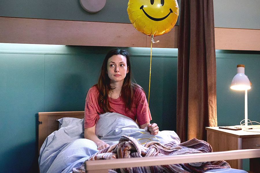 Gaite Jansen als Emma in PAAZ (2026), een film van Anne de Clercq, naar het boek van Myrthe van der Meer. Emma zit rechtop in een ziekenhuisbed, dekens over haar heen, in haar linkerhand heeft ze een ballon met een smiley face. Zelf kijkt ze verward, met een blik van "Wat doe ik hier?"